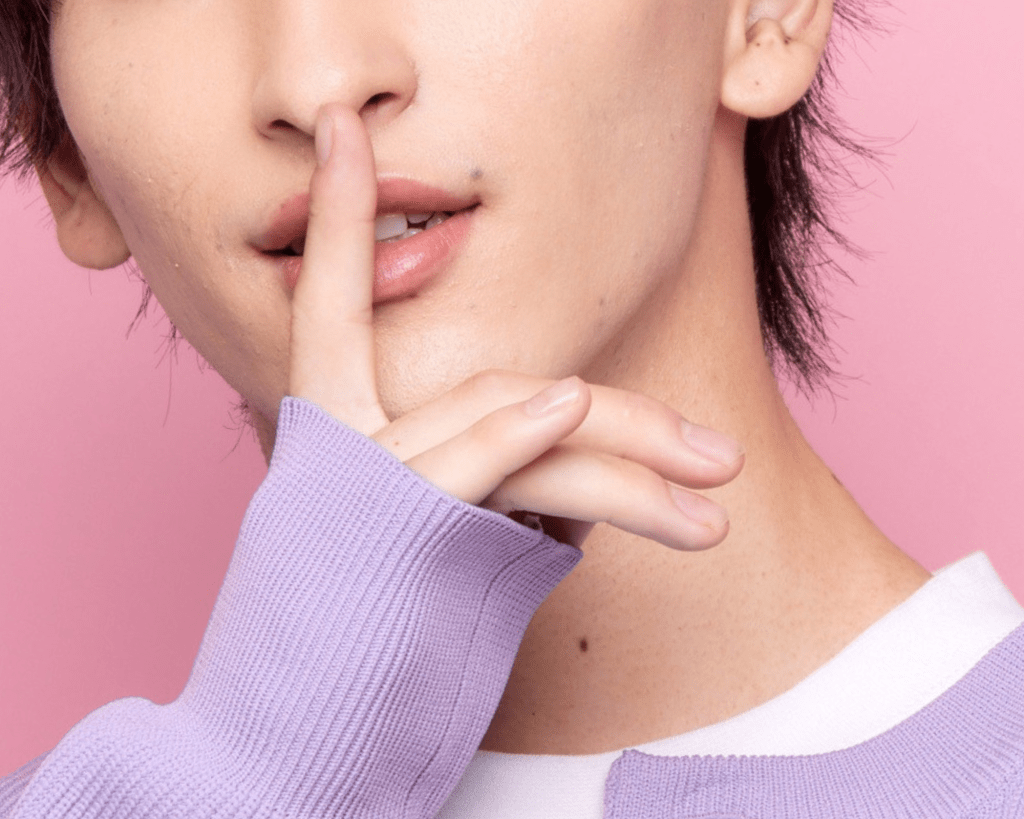 Man shushing with a purple sweater and pink background about the men's only arcade