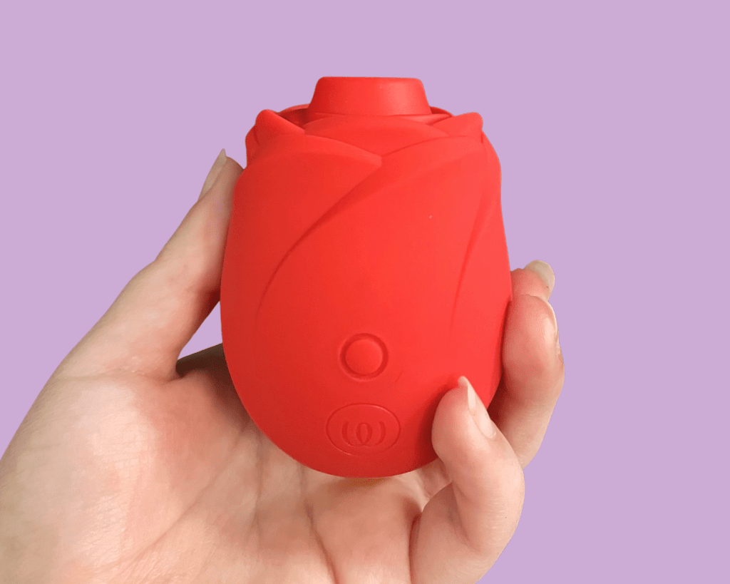 Hand holding a red rose sex toy with light purple background